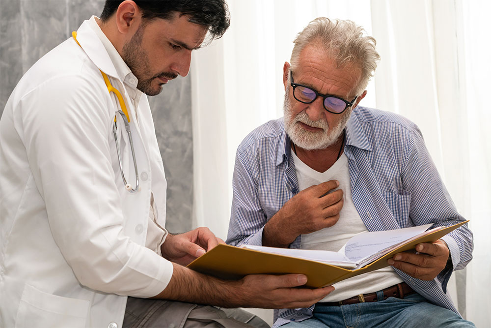 A male doctor shows a male patient treatment options for prostate cancer in a binder.